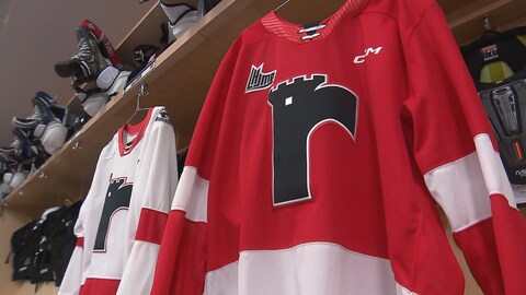 Le logo classique des Remparts apparaît sur un chandail uni rouge orné de bandes blanches. 