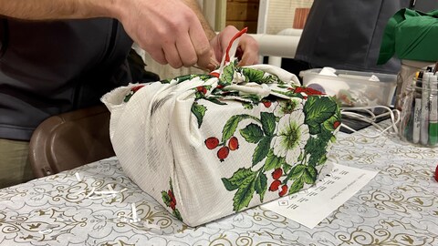 Une personne emballe un cadeau avec un tissu et un élastique.