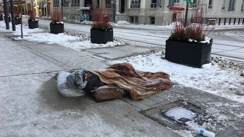 Un sans-abri dort dans la rue à Toronto, entouré de glace et de neige.