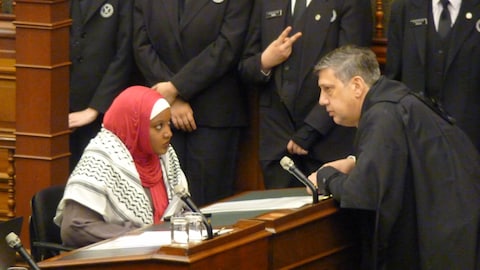 Sarah Jama, wearing the keffiyeh, seated at her desk, with the clerk facing her.
