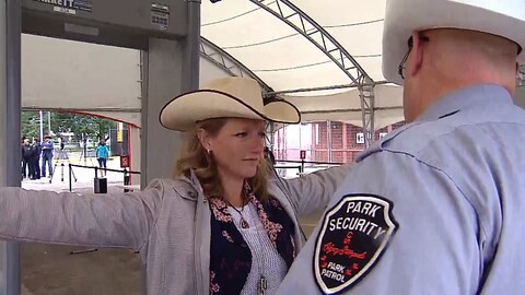 Un agent de sécurité scanne une femme avec un chapeau de cowboy à l'aide d'un détecteur de métal portatif. Derrière eux se trouve un portique de détection situé sous la tente à l'entrée du Stampede de Calgary. Un agent de sécurité scanne une femme avec un chapeau de cowboy à l'aide d'un détecteur de métal portatif. Derrière eux se trouve un portique de détection situé sous la tente à l'entrée du Stampede de Calgary.