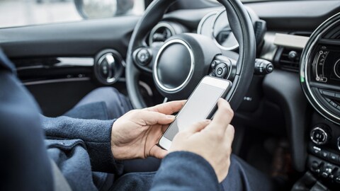 Une personne utilise son cellulaire alors qu'elle se trouve derrière le volant de sa voiture.