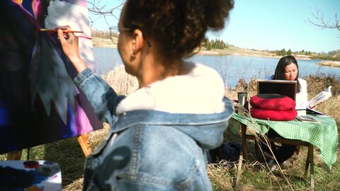 Sur le bord d'un lac à Regina en Saskatchewan, l'artiste visuelle Diana Ntibandetse peint pendant que la poète Thuy Nguyen écrit. 