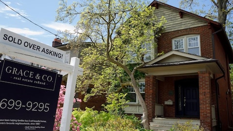 A sold-over-asking sign in front of a brick house.