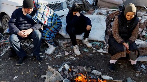 People sit next to a fire near the site of a collapsed building following an earthquake in Kahramanmaras, Turkey on Feb. 7, 2023. (Suhaib Salem/Reuters)