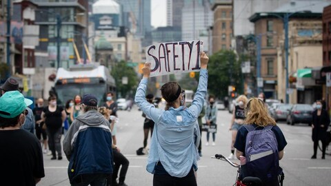 People, with their backs to the camera, protest in the street, one person holding a sign above their head.