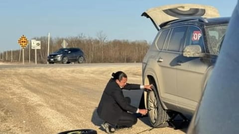 Le premier ministre, en costume-cravate, qui s'active à changer un pneu sur le bord de la route.