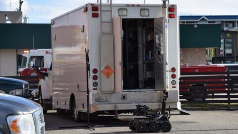 Un petit robot sur chenilles devant un grand camion dans un stationnement, avec en arrière-plan un camion de pompiers. Un petit robot sur chenilles devant un grand camion dans un stationnement, avec en arrière-plan un camion de pompiers.