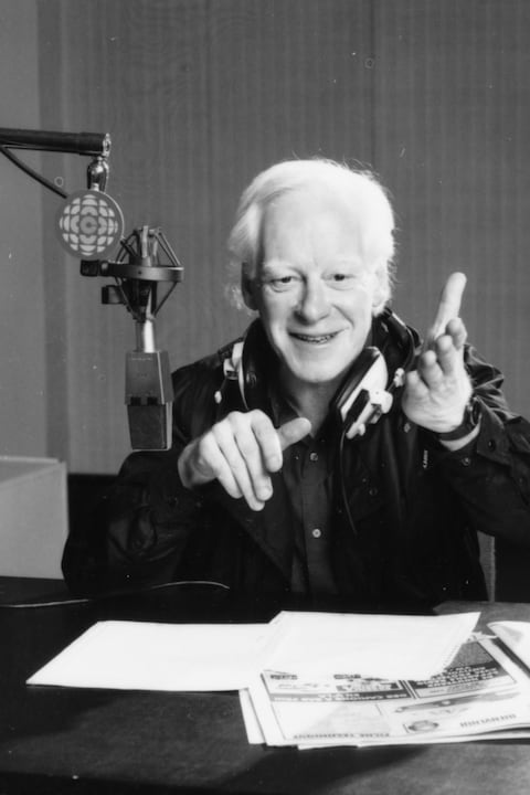 L'animateur Pierre Bourgault, des écouteurs encerclant son cou,
est assis à une table où reposent ses notes qu'il tient d'une main. Près de sa tête, on voit un micro suspendu qui porte une affichette
avec le logo de Radio-Canada. L'animateur Pierre Bourgault, des écouteurs encerclant son cou,
est assis à une table où reposent ses notes qu'il tient d'une main. Près de sa tête, on voit un micro suspendu qui porte une affichette
avec le logo de Radio-Canada.