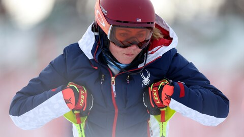 Une jeune femme casquée s'appuie sur ses bâtons de ski avec l'air pensif. 