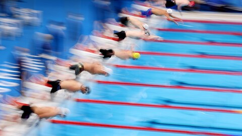 Des nageurs se lancent dans la piscine au début d'une épreuve des Jeux olympiques. On ne les distingue pas vraiment, ils sont flous. 