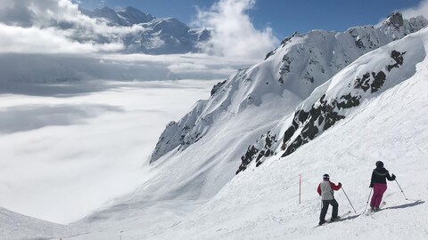 Deux skieurs sont arrêtés dans une piste. Ils regardent le paysage au loin.