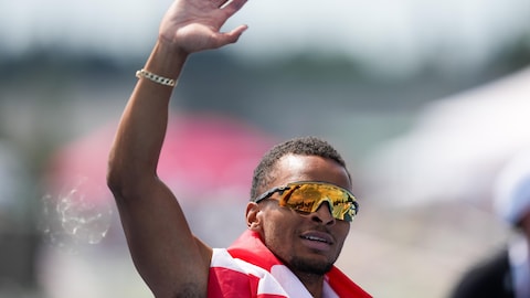 Drapé d'un drapeau canadien, un athlète salue la foule.