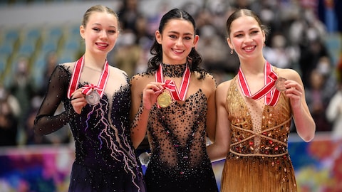 Trois patineuses en costume sourient et montrent leurs médailles.