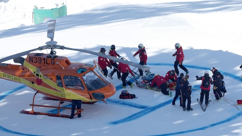 Des secouristes entourent un skieur couché au sol, tout près d'un hélicoptère de secours.