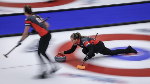 Une joueuse de curling lance une pierre pendant un match, sous le regard d'une coéquipière.