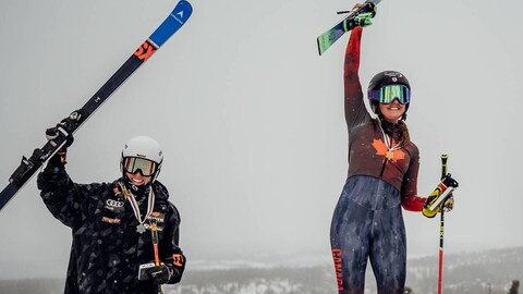 Deux skieuses casquées lèvent leurs skis et sourient, avec leurs médailles autour du cou. 