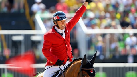 Un cavalier en rouge lève le poing en triomphe sur son cheval.