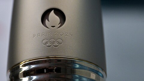 Gros-plan d'un cylindre métallique orné des anneaux olympiques, de l'emblème des Jeux de 2024 et et de l'inscription «Paris 2024» 