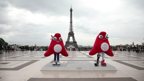 Deux mascottes se tiennent sur un podium avec les anneaux olympiques. La tour Eiffel se trouve au loin.