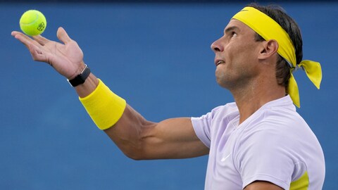 Le joueur de tennis s'apprête à lancer la balle dans les airs pour effectuer son service.