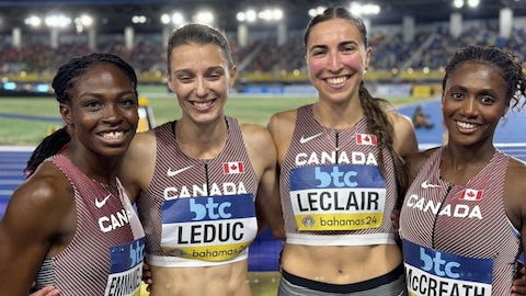 Quatre femmes se tiennent par la taille et sourient pour la caméra. Elles sont en bordure d'une piste d'athlétisme.