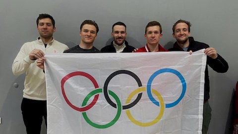 Les cinq escrimeurs sont alignés et tiennent un drapeau avec les anneaux olympiques.