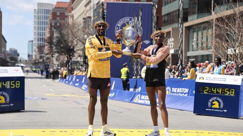 Deux coureurs, un homme et une femme, tiennent un trophée sur la ligne d'arrivée d'un marathon.