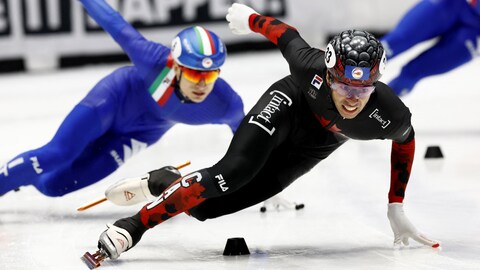 Un patineur de vitesse sur courte piste effectue un virage devant un adversaire.