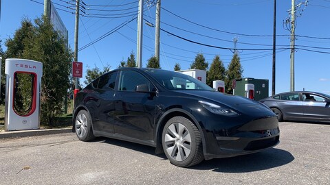 Une voiture électrique stationnée devant une borne de recharge Tesla.