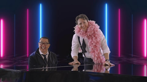 Les deux personnages devant un piano, avec des néons derrière eux.