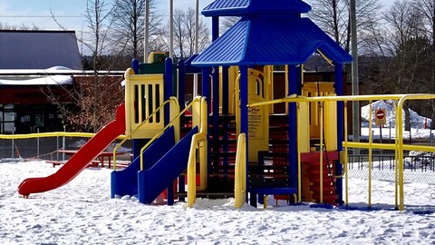 Un terrain de jeux et des balançoires en hiver et le bâtiment principal de l'école au loin.