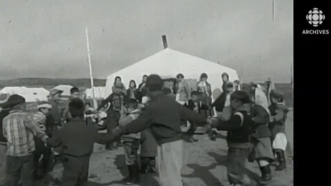 Image en noir et blanc de jeunes Autochtones dansant près d'une tente.  