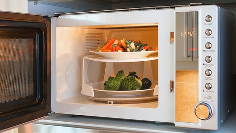 Un micro-onde avec deux assiettes à l'intérieur, l'une avec une macédoine de légumed, l'autre avec des brocolis