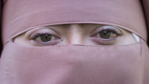 Une femme en niqab rose, vue en gros plan, regarde droit dans la caméra.