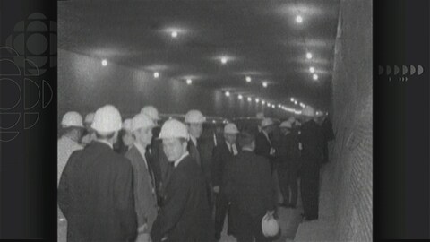 Photo en noir et blanc sur laquelle on voit plusieurs hommes en complet-cravate portant un casque de construction, à l'intérieur du tunnel Louis-Hippolyte-Lafontaine