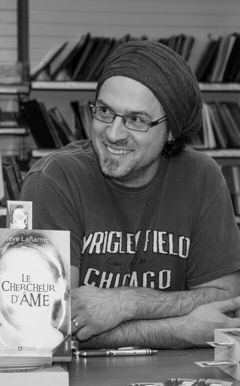 L'écrivain Steve Laflamme lors d'une séance de signature pour son premier roman Le chercheur d'âme. l'auteur est assis derrière une table, souriant. Sur la table on voit son livre. L'écrivain Steve Laflamme lors d'une séance de signature pour son premier roman Le chercheur d'âme. l'auteur est assis derrière une table, souriant. Sur la table on voit son livre.
