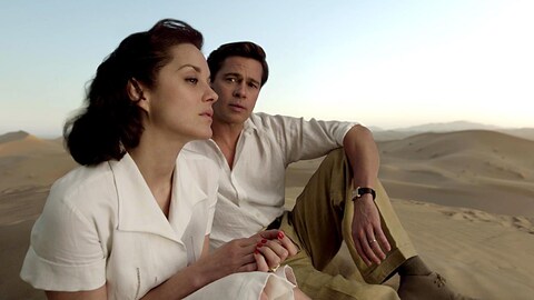 Un homme (Brad Pitt) et une femme (Marion Cotillard) assis dans des dunes de sable.