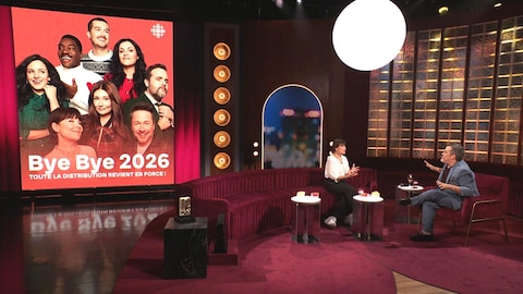 Karine Dufour/La production est encore jeune La comédienne Anne Dorval en entrevue avec Jean-Sébastien Girard, assise dans un canapé sur le plateau de Bonsoir bonsoir. Une photo de la distribution du Bye bye est affichée sur un grand écran.