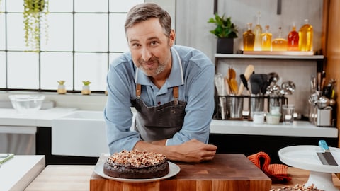 Le chef cuisinier pose avec son gâteau dans la cuisine.