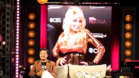 La production est encore jeune / Karine Dufour Sébastien Diaz est assis sur le plateau de Bonsoir bonsoir. Une image de Dolly Parton est diffusée derrière lui.