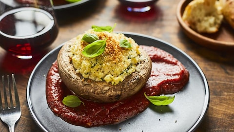 Un champignon portobello farci et gratiné, disposé sur une sauce tomate dans une assiette.