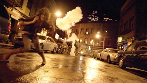 Une jeune fille court dans une rue, la nuit, devant plusieurs explosions.