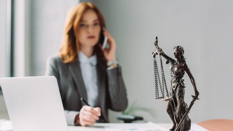 Une avocate parle au téléphone, avec en avant-plan une statue de la déesse de la justice.