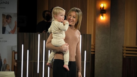 Dominique Bernèche tient un bébé dans ses bras sur le plateau de l'émission Dans l'oeil du dragon.