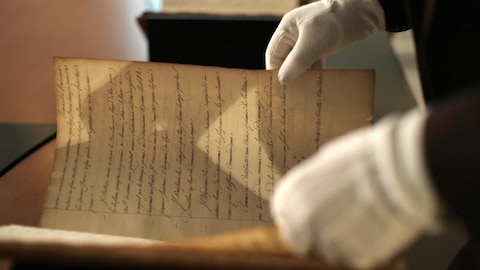 Une personne ouvre un vieux manuscrit datant de l'époque de la Nouvelle-France.