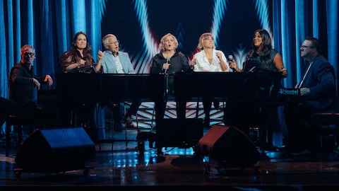 France Castel, Véronique Claveau et Mélissa Bédard chantent autour du piano.