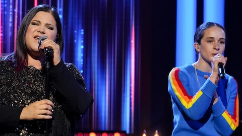 La chanteuse et la rappeuse regardent le public, micro à la main.