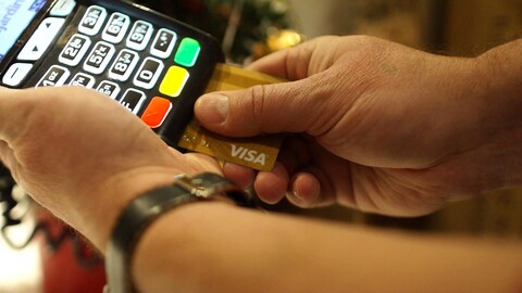 Des mains manipulent un terminal de carte de crédit pour une transaction avec une carte Visa