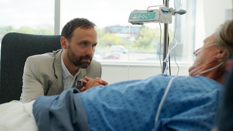 François tient la main de Michel, qui est dans un lit d'hôpital.